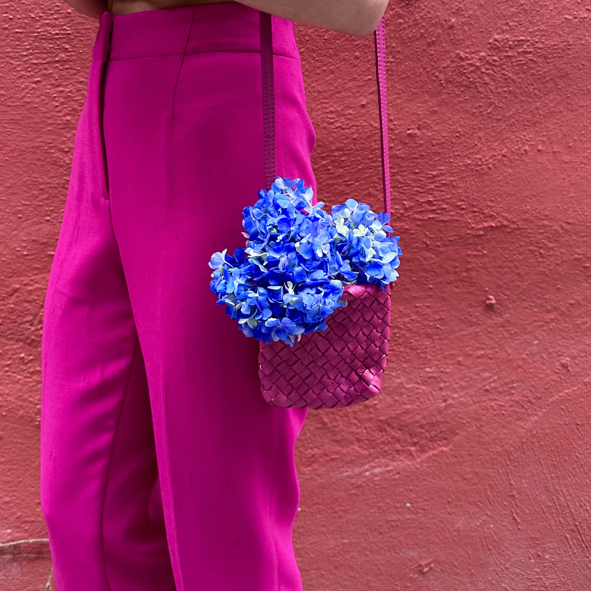 Art inspired fashion look with pink pants against a pink wall and a blue hydrangea sitting in the purse.  