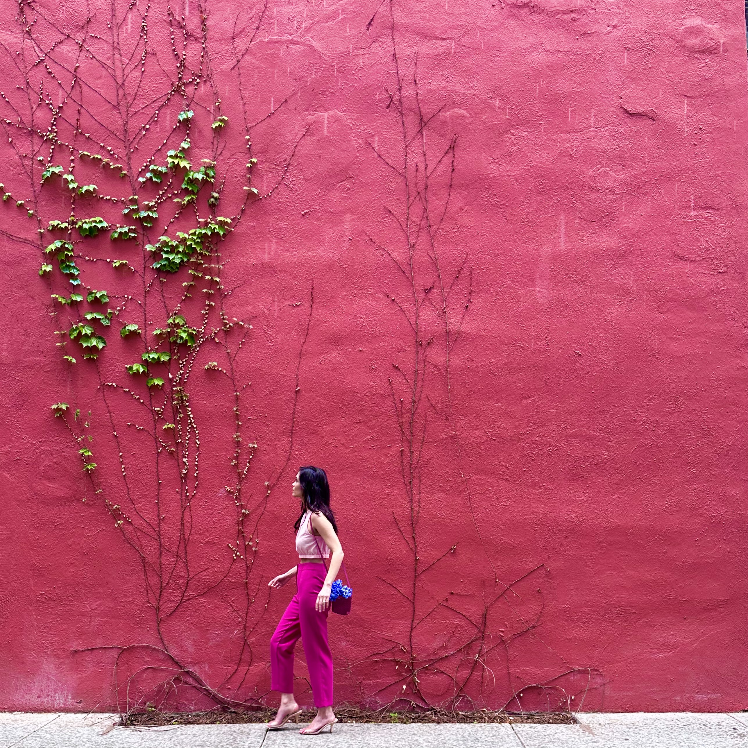Stylish girl walks by a pink wall wearing a pink outfit to articulate the connection between art and fashion. 